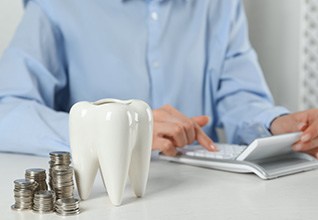 A patient using a calculator next to a large model tooth and stacks of silver coins