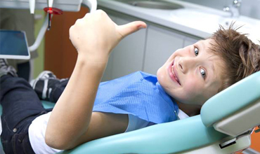 child in dental chair giving thumbs up