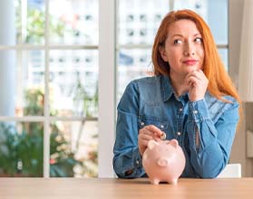 Woman putting coin in piggy bank for dental implants in Chevy Chase