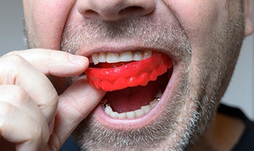 close up of man with short facial hair putting a red sportsguard into his mouth 