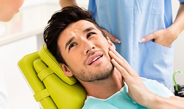 Young man in dental chair in pain holding face
