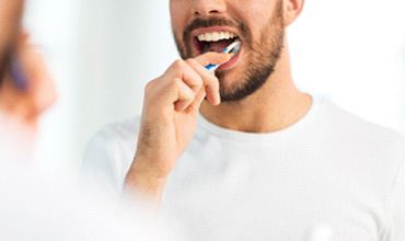 Closeup of man in white shirt brushing his teeth