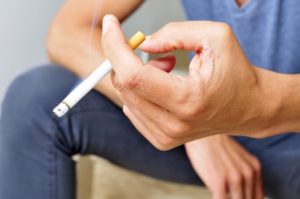 Man with dental implants in Chevy Chase holding a cigarette. 