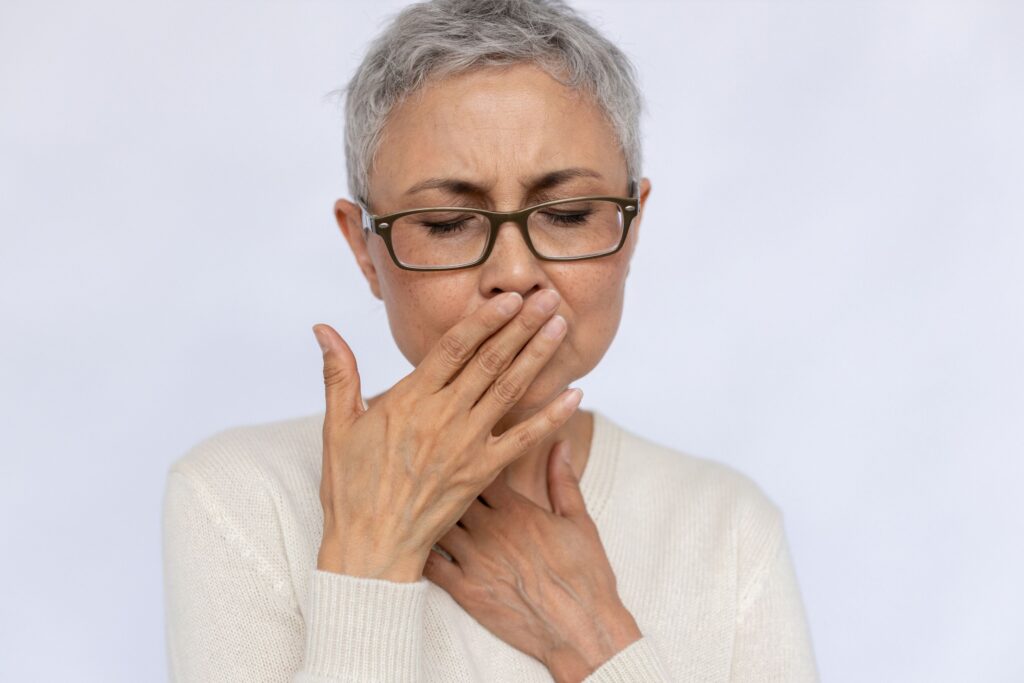 Woman with short gray hair holding hands over mouth with eyes closed